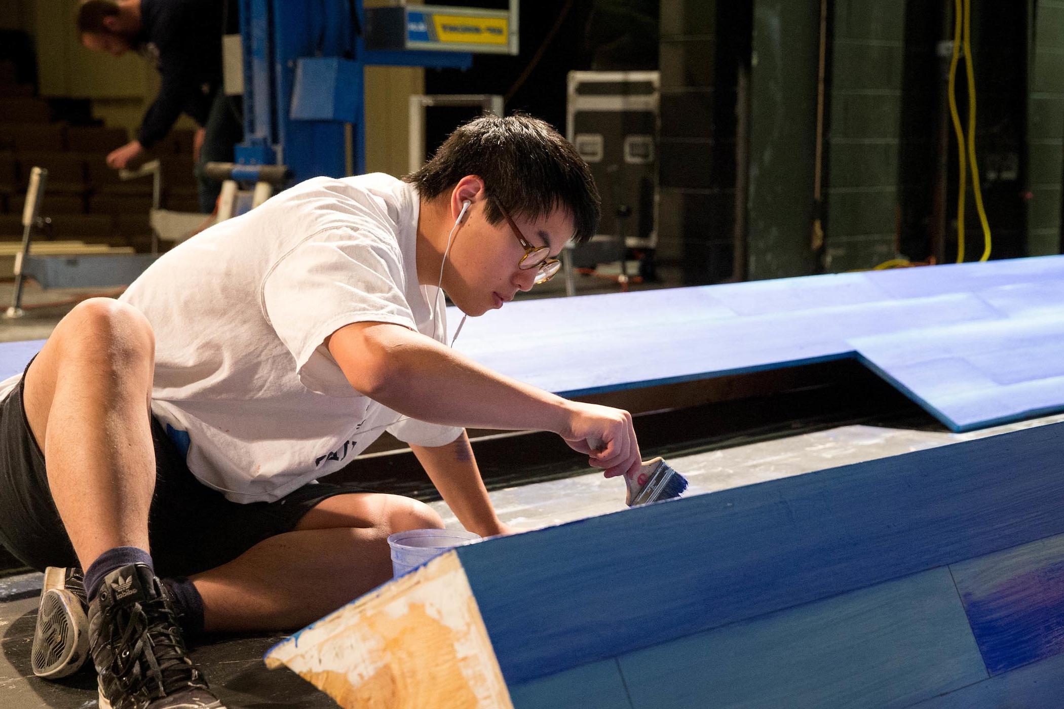 Male student paints stage scenery.
